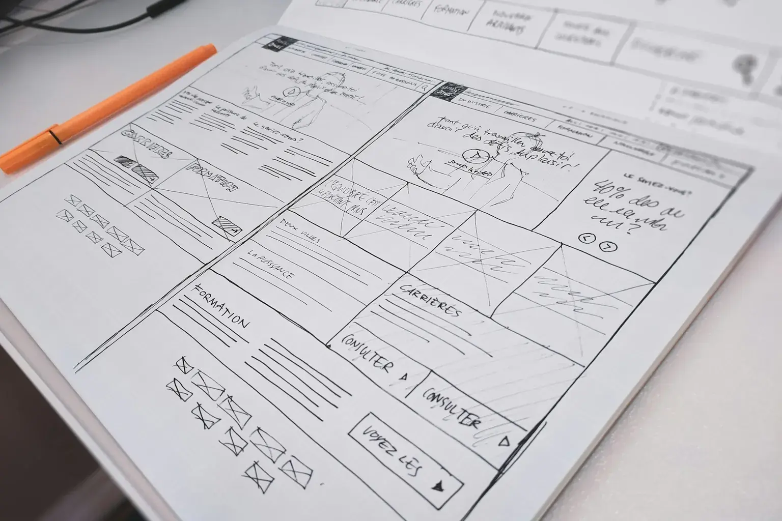 Hand-drawn website wireframe on paper with an orange pen